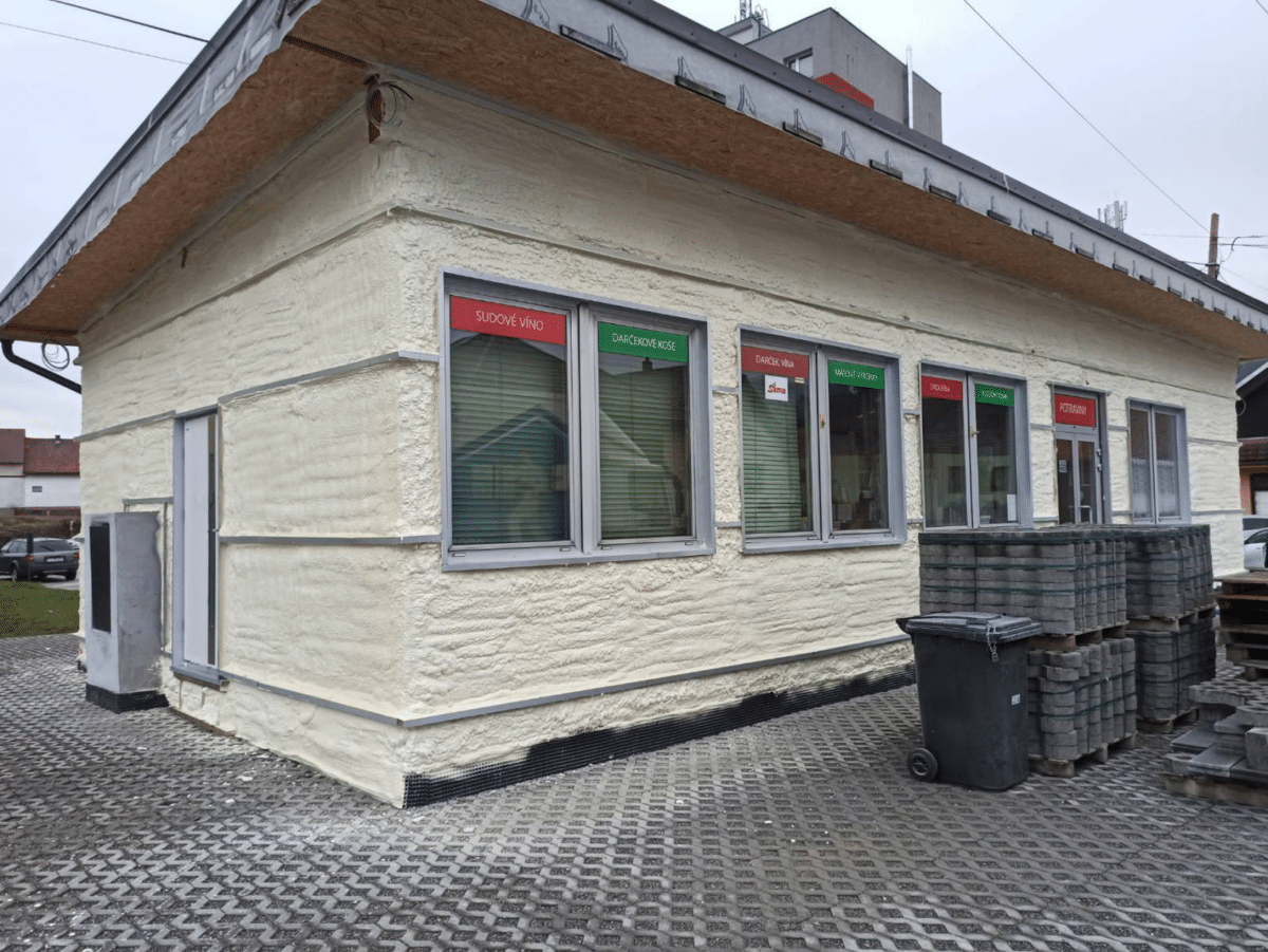 Prev&aacute;dzkov&aacute; budova s bielou fas&aacute;dou a niekoľk&yacute;mi obchodn&yacute;mi prev&aacute;dzkami.